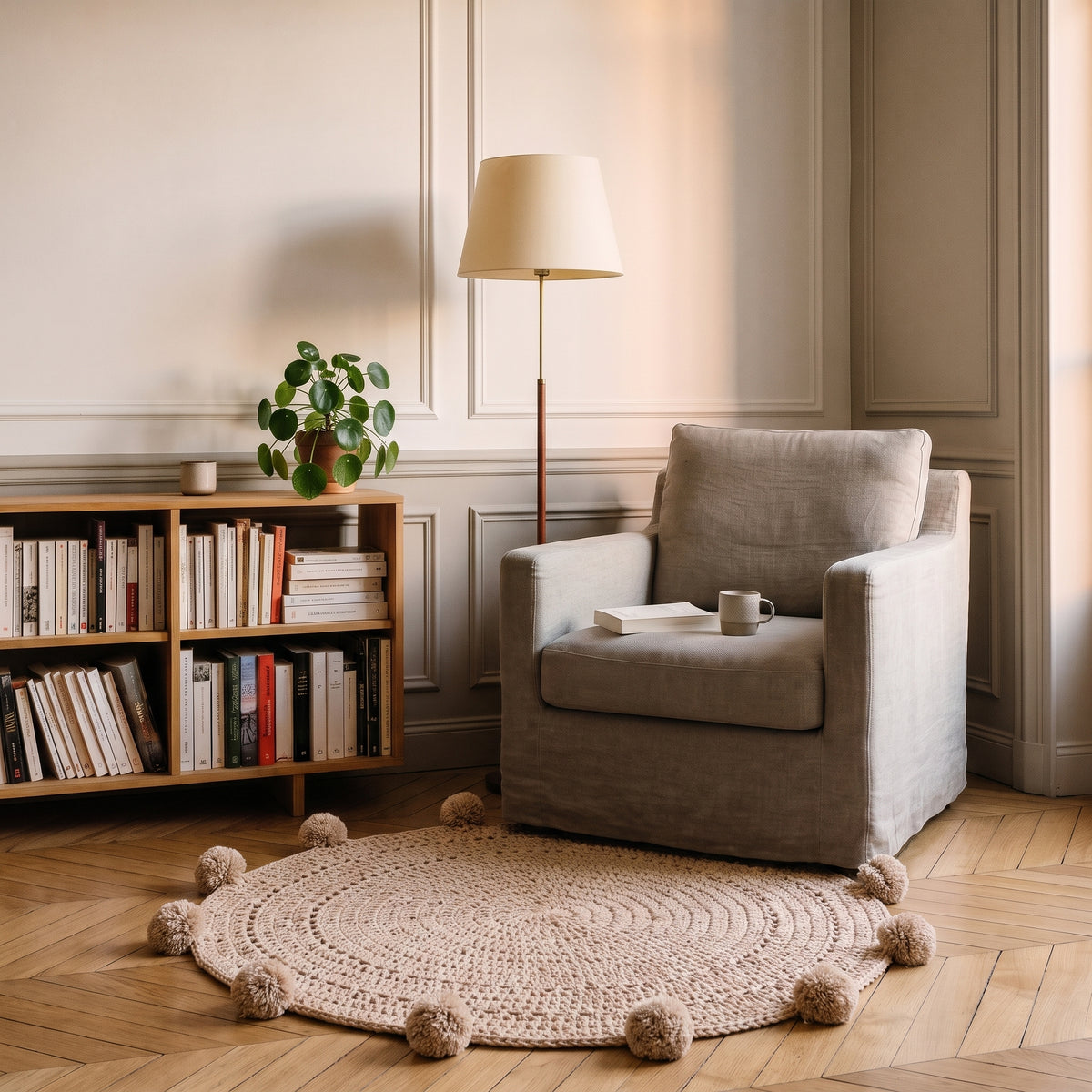 Tapis rond beige à pompons au pied d’un fauteuil dans un coin lecture