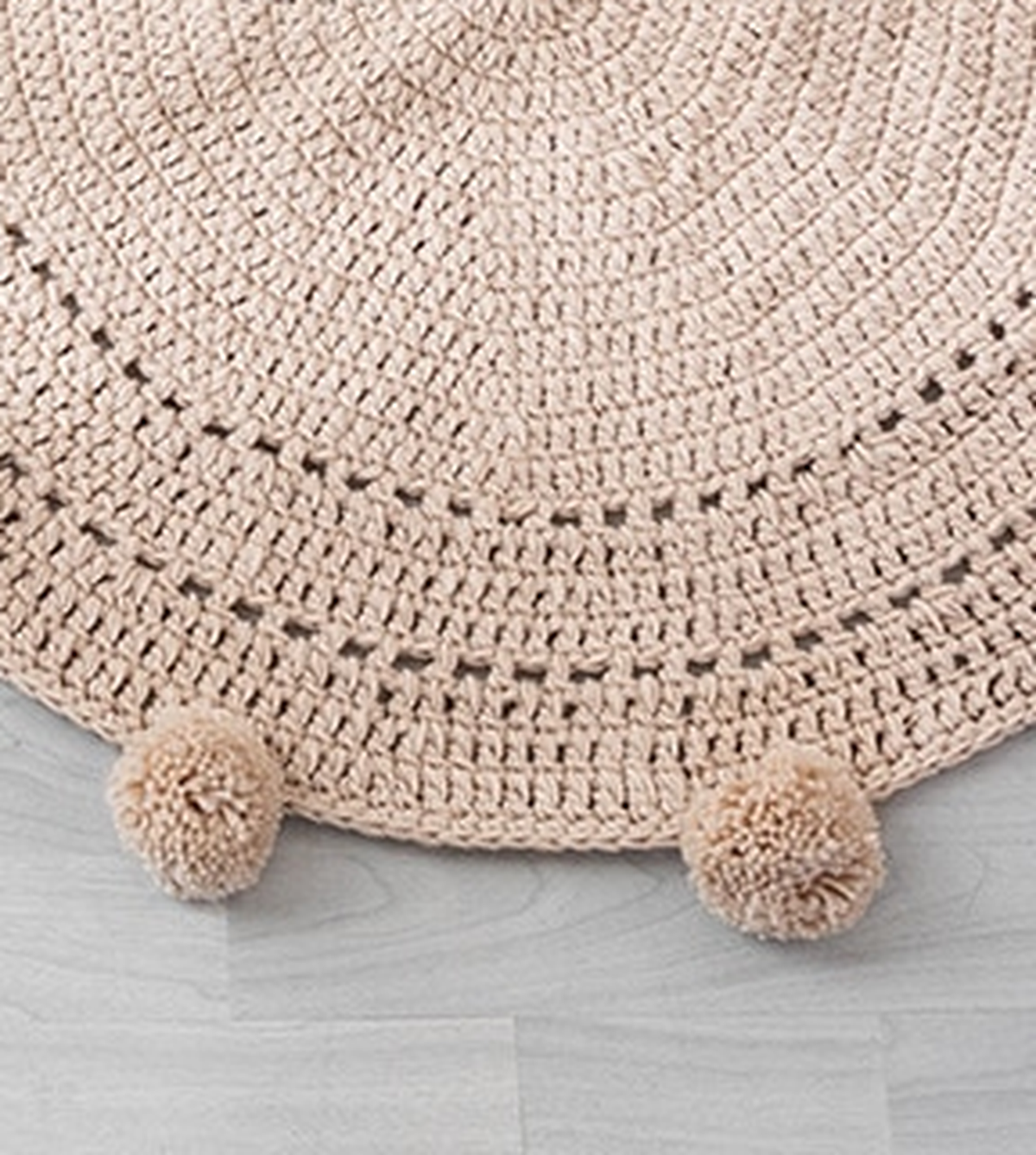 Gros plan sur la bordure à pompons et le tissage ajouré du tapis rond beige
