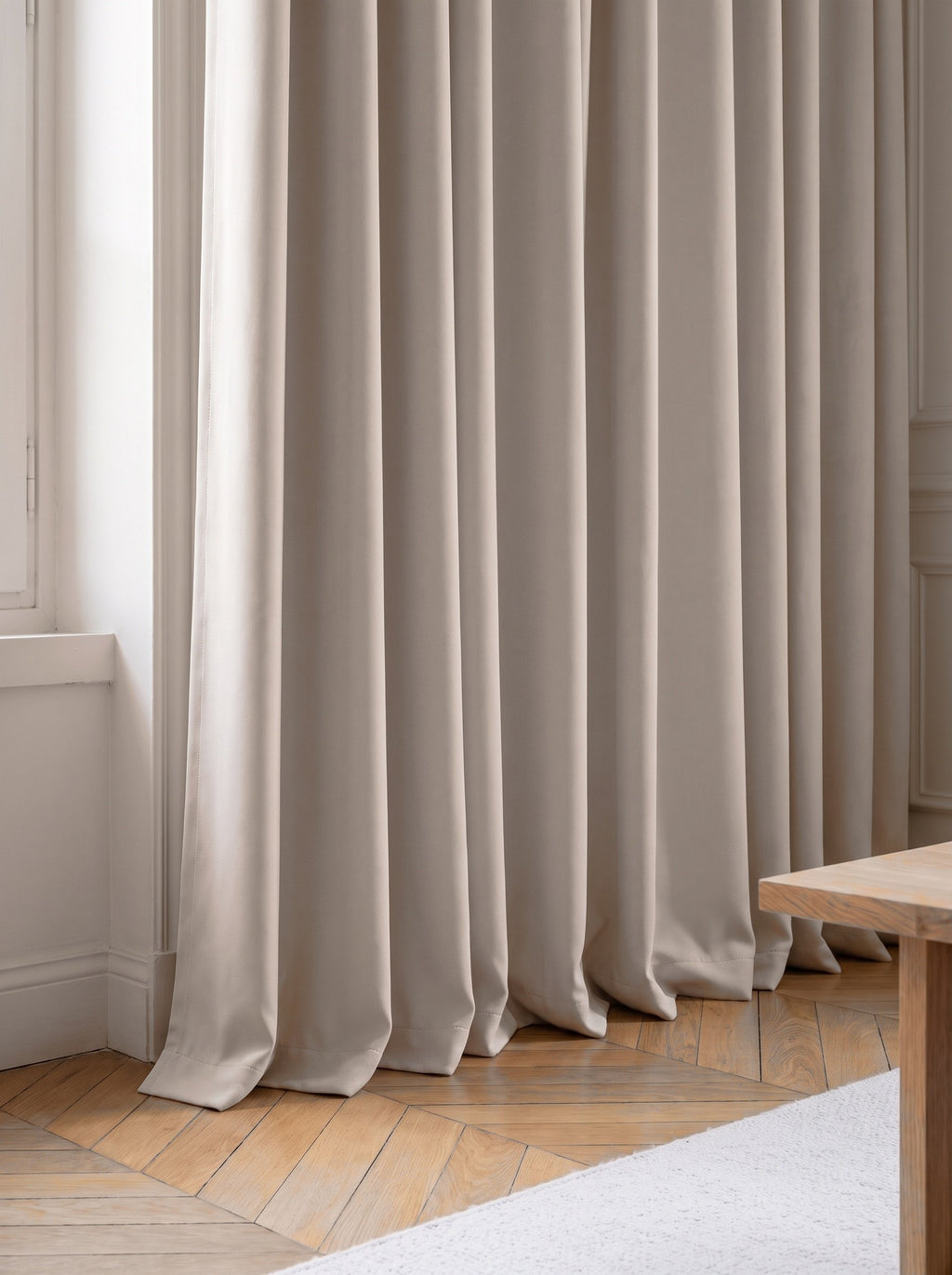 Ourlet d'un rideau occultant uni beige posé sur un parquet en point de Hongrie