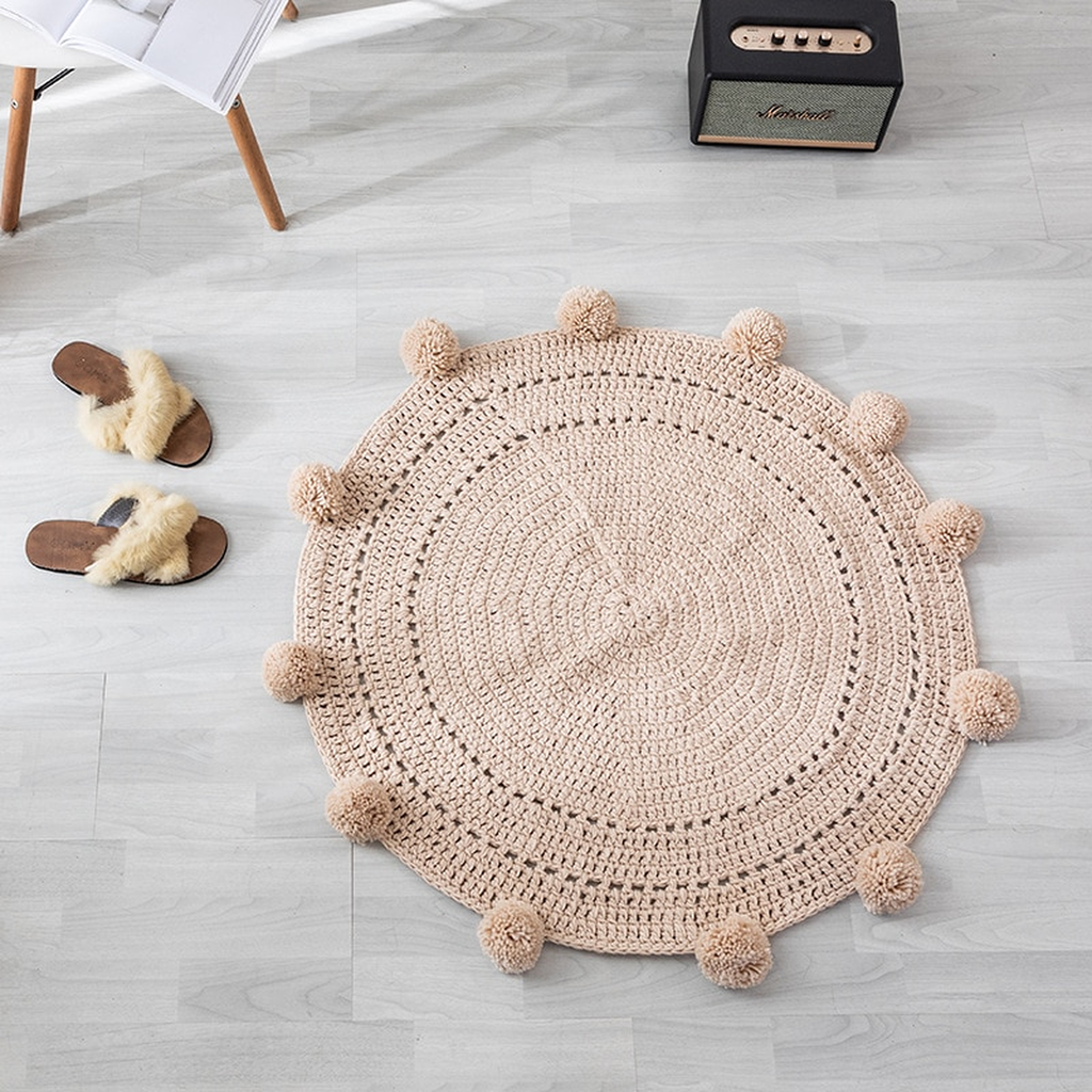 Tapis rond beige à pompons vu de dessus, posé sur un parquet clair