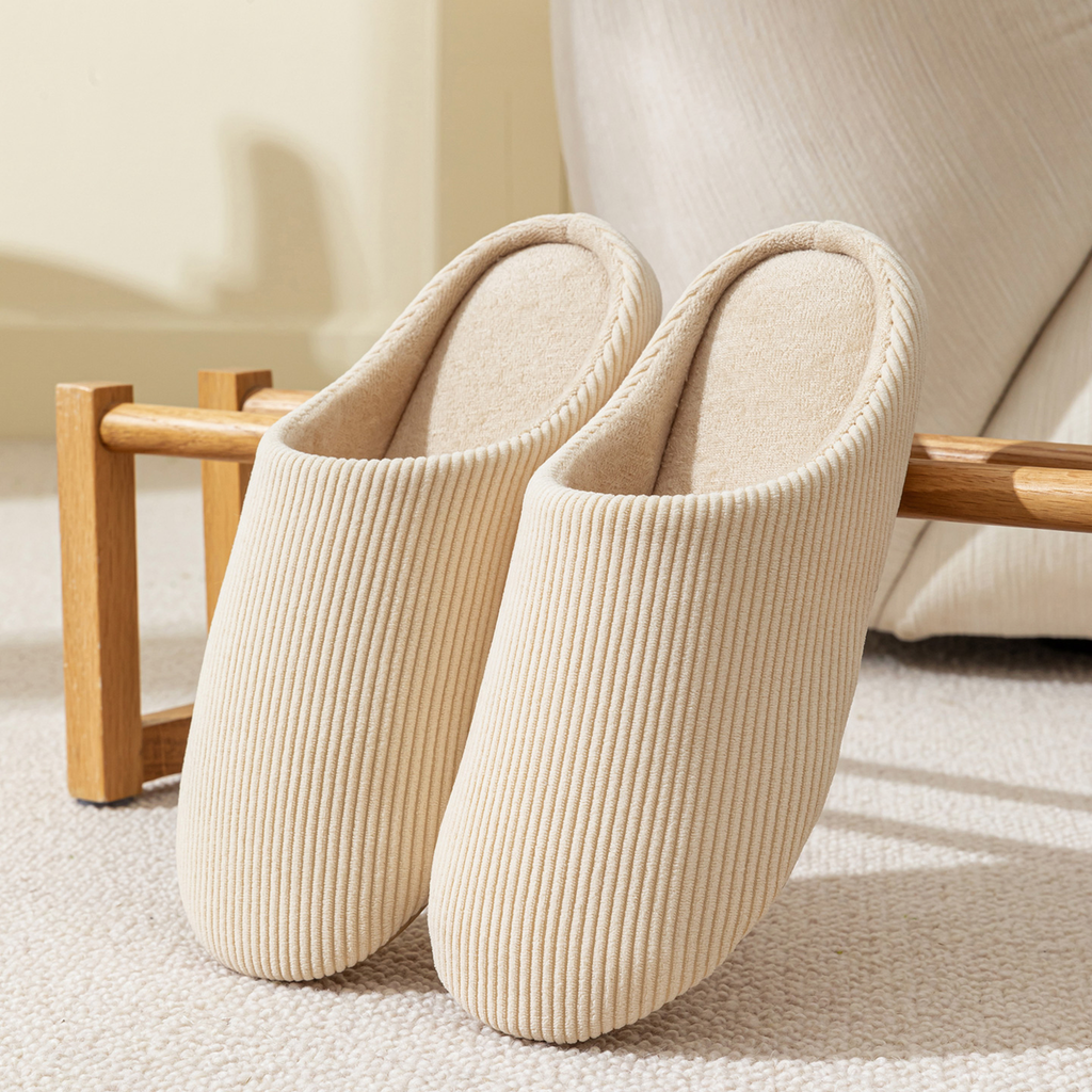 Paire de chaussons homme beige en velours côtelé posée dans un salon chaleureux