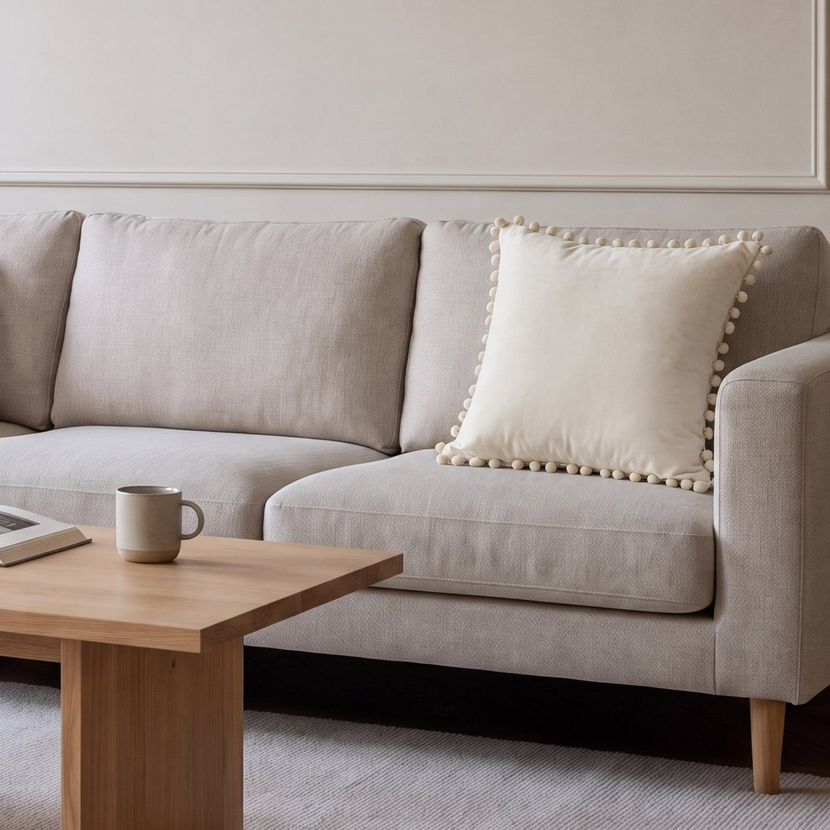 Housse de coussin en velours beige à pompons posée sur un canapé écru