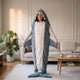 Femme debout portant le plaid requin bleu-gris, capuche relevée, les bras hors du sac, dans un salon