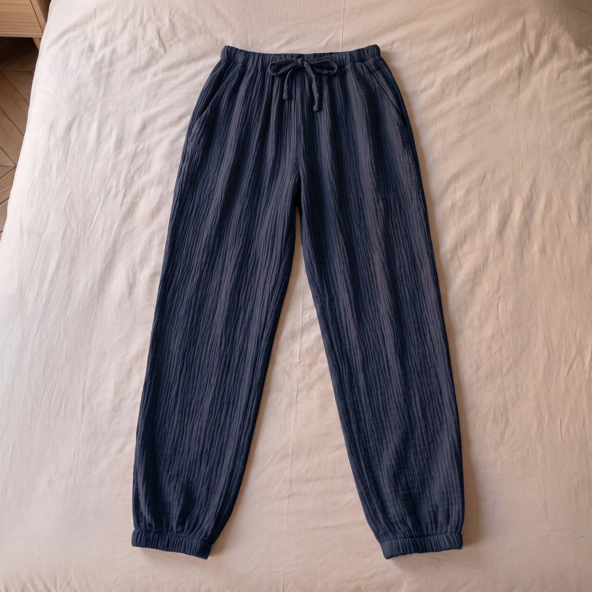 Pantalon de pyjama bleu marine en gaze de coton pose a plat sur la literie, vu du dessus