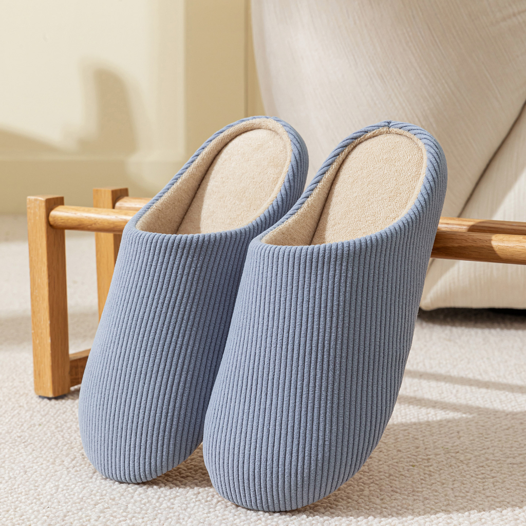 Paire de chaussons homme bleu en velours côtelé posée dans un salon chaleureux
