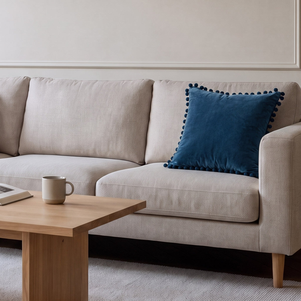 Housse de coussin en velours bleu à pompons posée sur un canapé écru