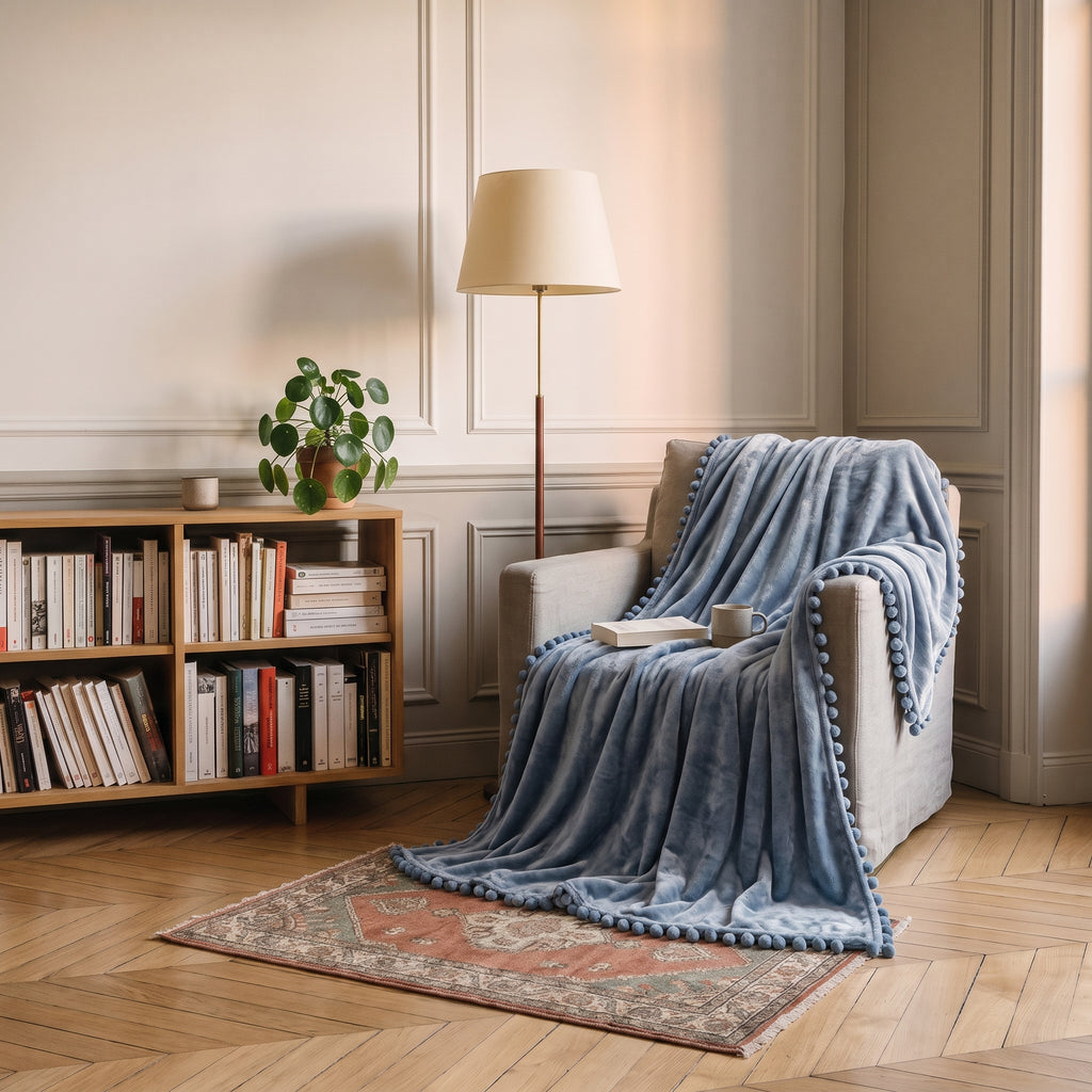 Plaid molletonné bleu gris à pompons posé sur un fauteuil de lecture
