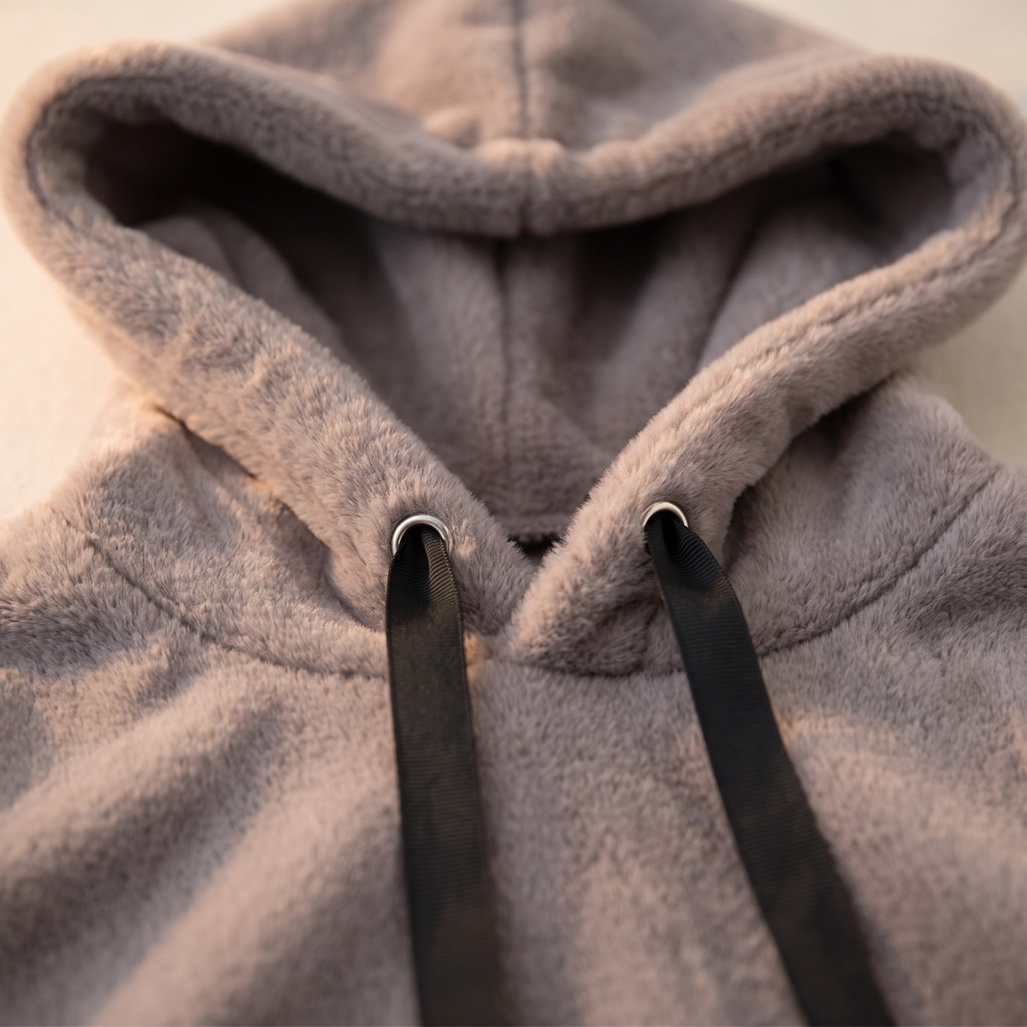 Gros plan sur l encolure du sweat gris : les deux oeillets metalliques argentes, le ruban plat noir qui les traverse et la capuche doublee de la meme peluche Image