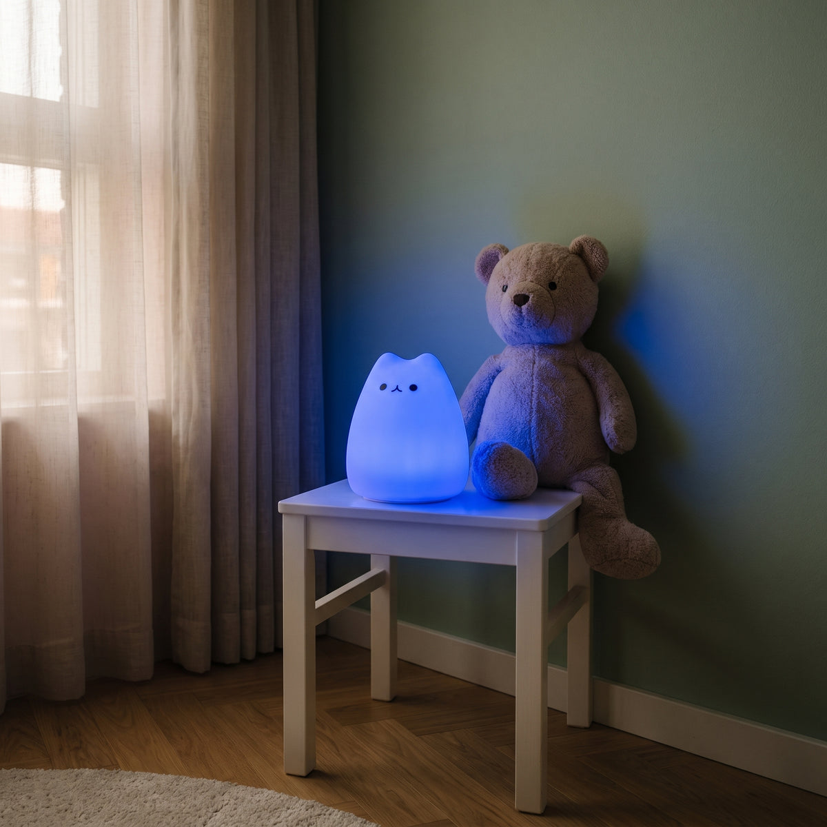 Veilleuse chat allumée en bleu sur le tabouret de chevet, un ourson en peluche assis à côté Image