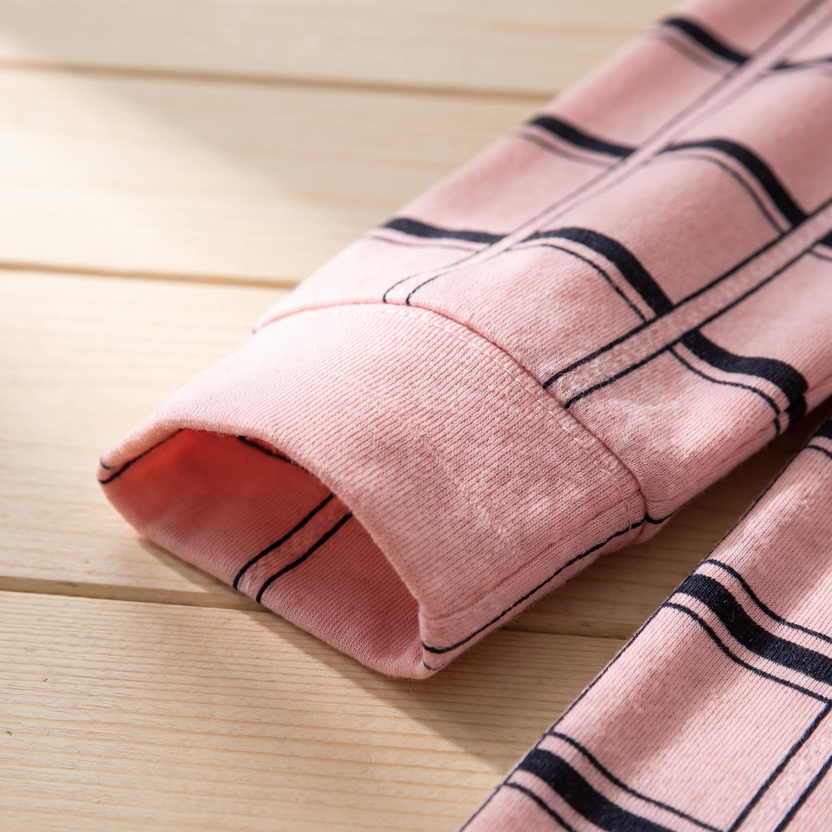 Gros plan du poignet et de la maille du pyjama rose a carreaux, en lumiere rasante. Image