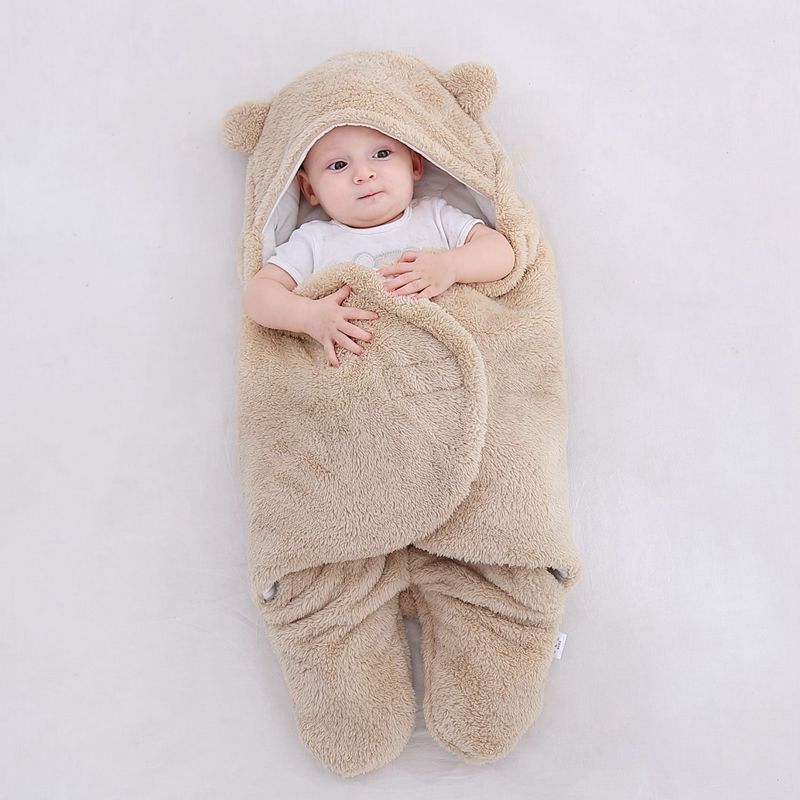 Bebe couche sur le dos dans la gigoteuse beige, capuche relevee autour du visage : le pan se referme sous ses aisselles et ses deux bras restent dehors, mains posees sur le tissu Image