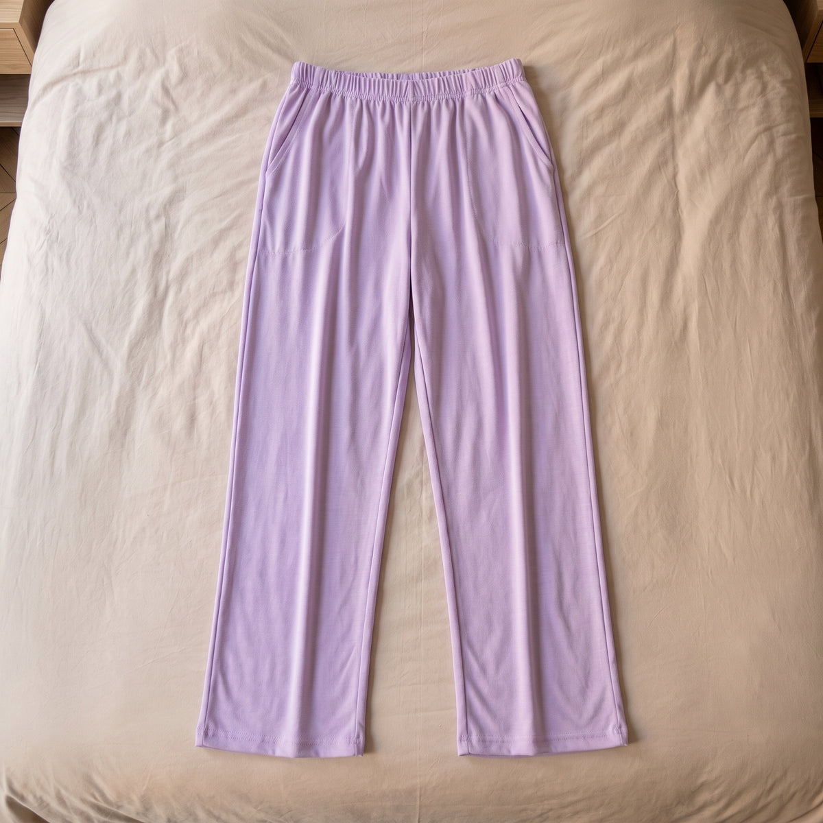 Le bas de pyjama lilas pose a plat sur le lit, vu du dessus en entier, de la ceinture a l ourlet des deux jambes. Image