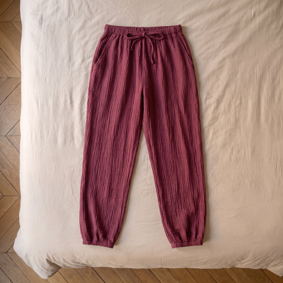 Pantalon de pyjama bordeaux en gaze de coton pose a plat sur le lit, vu du dessus