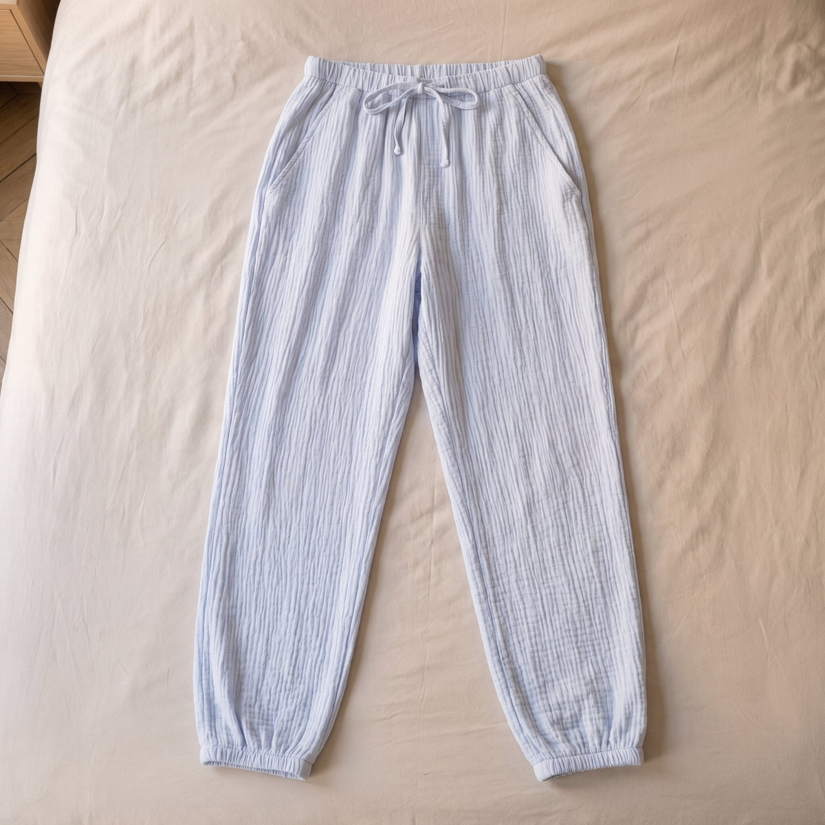Pantalon de pyjama bleu ciel en gaze de coton pose a plat sur le lit, vu du dessus
