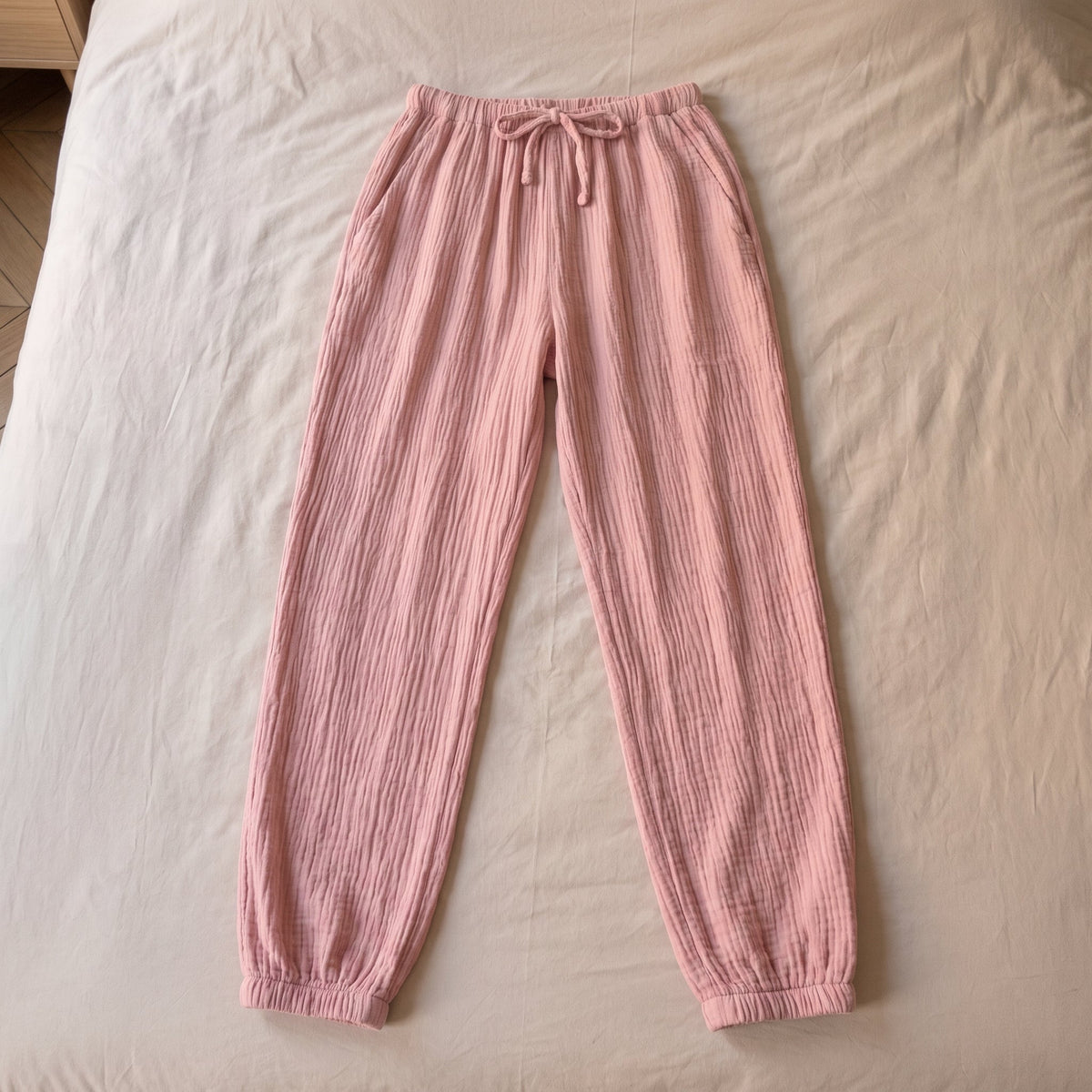 Pantalon de pyjama vieux rose en gaze de coton pose a plat sur le lit, vu du dessus