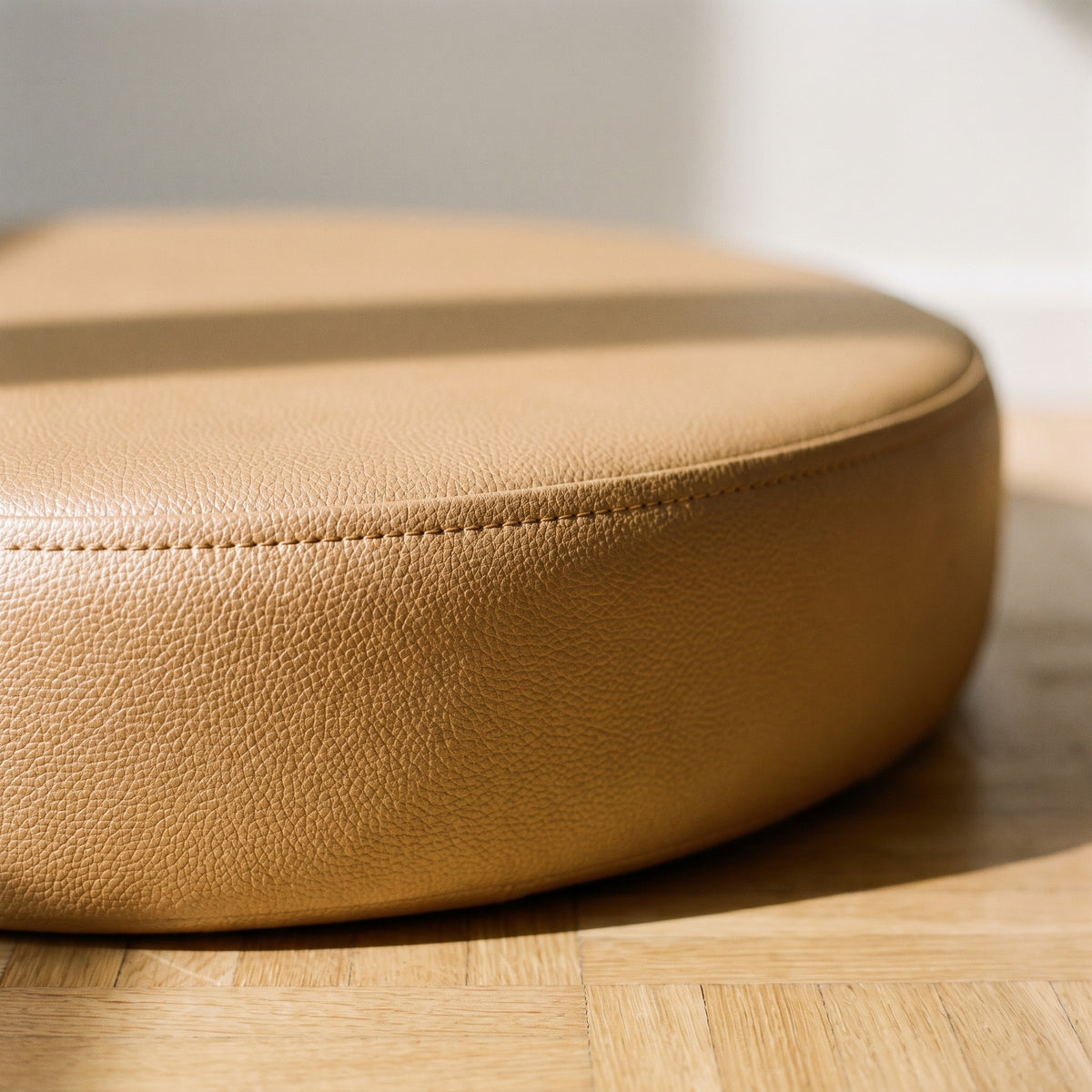 Gros plan sur le bord d'un coussin de sol camel, grain fin du simili cuir et piqûre courant sur l'arête de la tranche