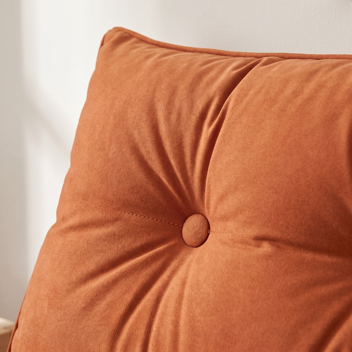 Gros plan sur un bouton capitonné d'un coussin de chevet terracotta, creux du capitonnage et grain mat du tissu