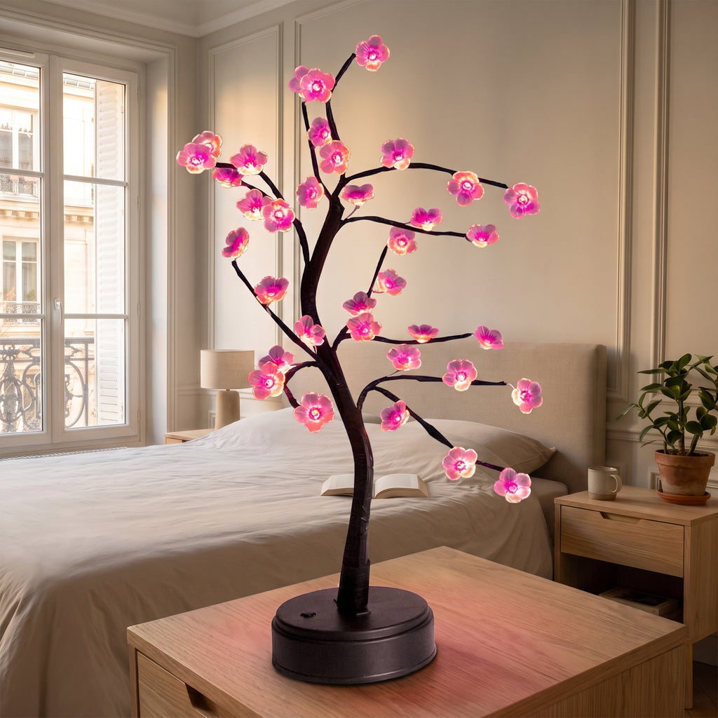 Lampe bonsaï LED à fleurs roses allumée sur des livres, sur une table de chevet en bois clair