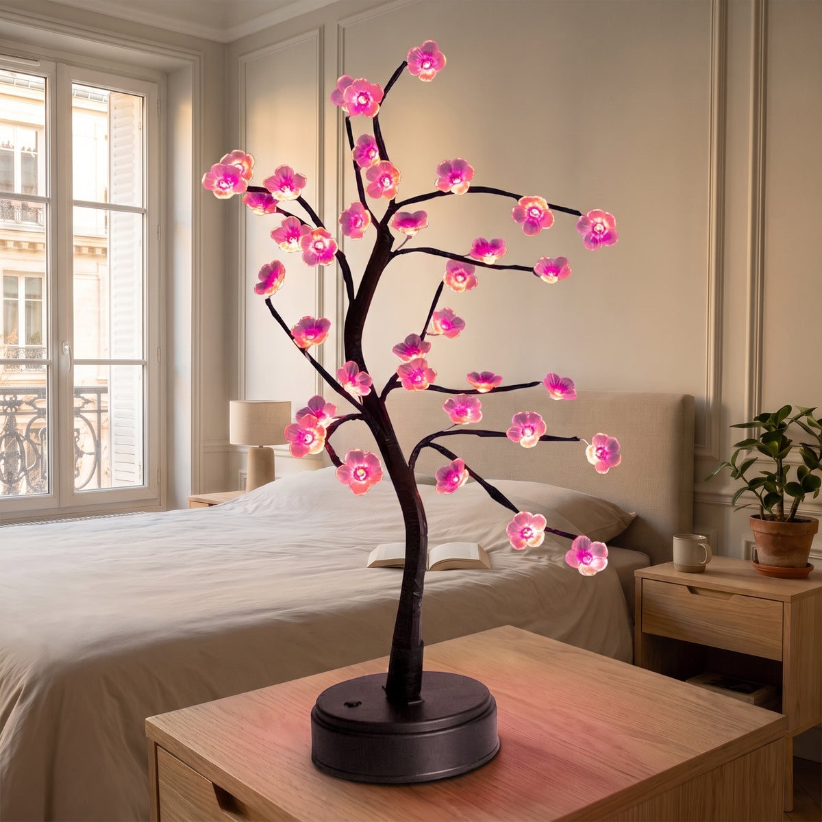Lampe bonsaï LED à fleurs roses allumée sur des livres, sur une table de chevet en bois clair