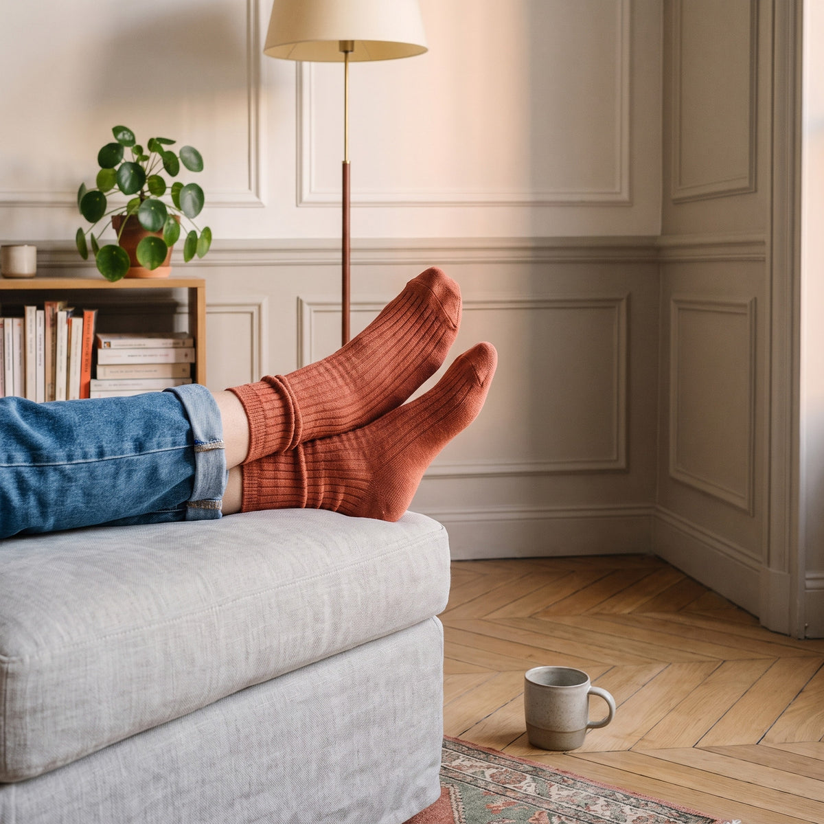 Pieds en chaussettes côtelées terracotta posés sur un pouf de coin lecture, jean roulé sur le mollet