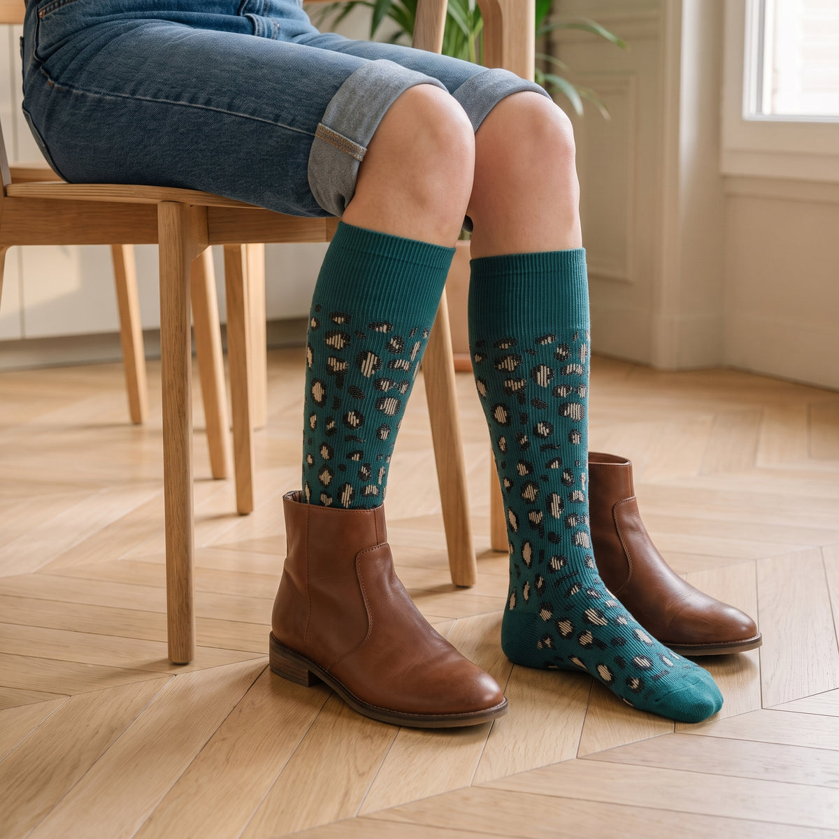 Assise au coin repas, chaussettes montantes vert canard jusque sous le genou : une bottine en cuir brun est enfilée par-dessus l'une d'elles, la seconde attend posée sur le parquet Image