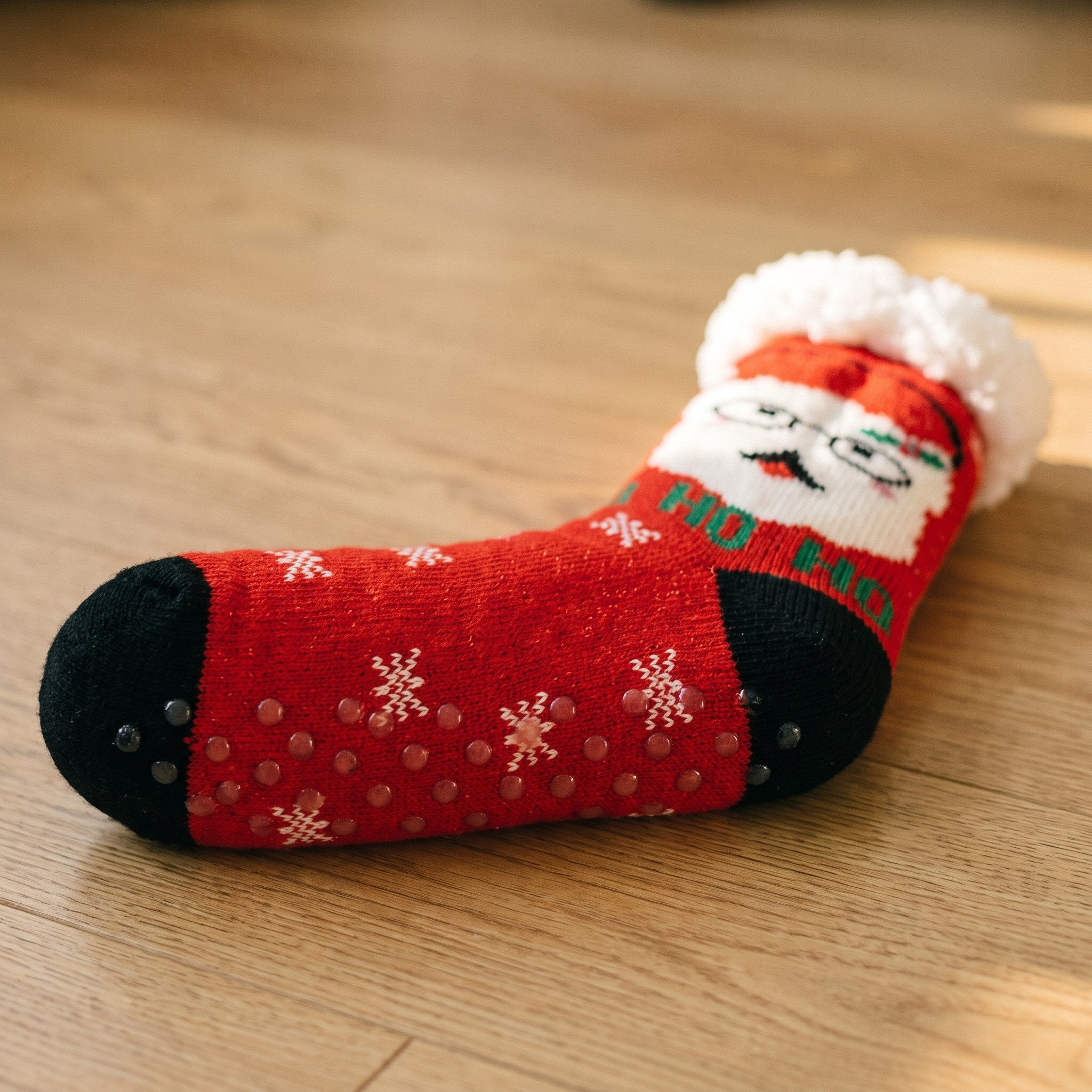 Semelle d'une chaussette de Noël rouge posée sur un parquet, ses billes de caoutchouc antidérapantes Image