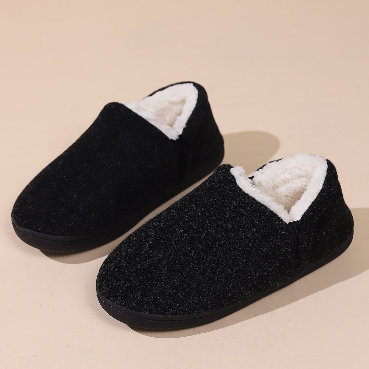 Paire de chaussons fermés fourrés noirs vue de trois quarts sur fond beige