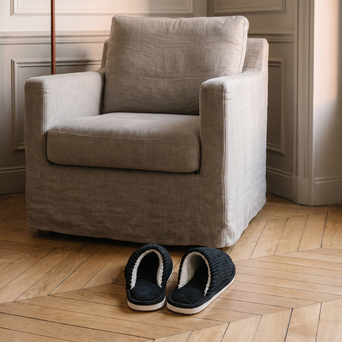 Chaussons noirs en velours côtelé posés devant le fauteuil du coin lecture