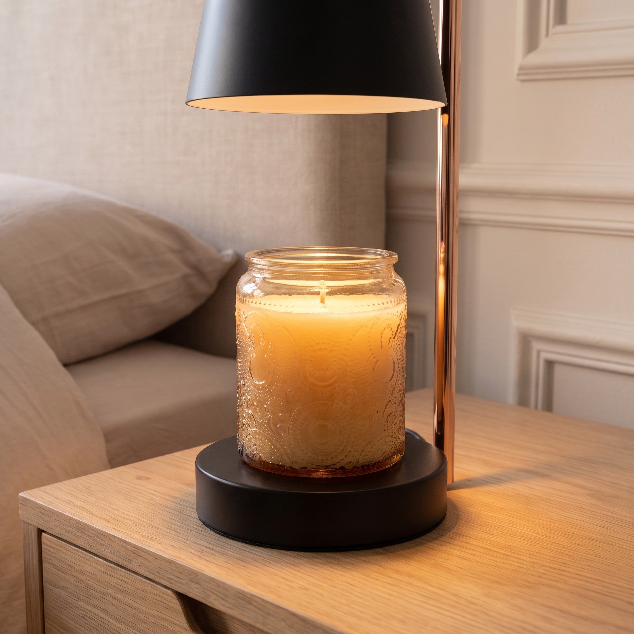 Socle noir de la lampe chauffe-bougie posé sur une table de chevet, un pot de bougie en verre au centre sous l'abat-jour Image