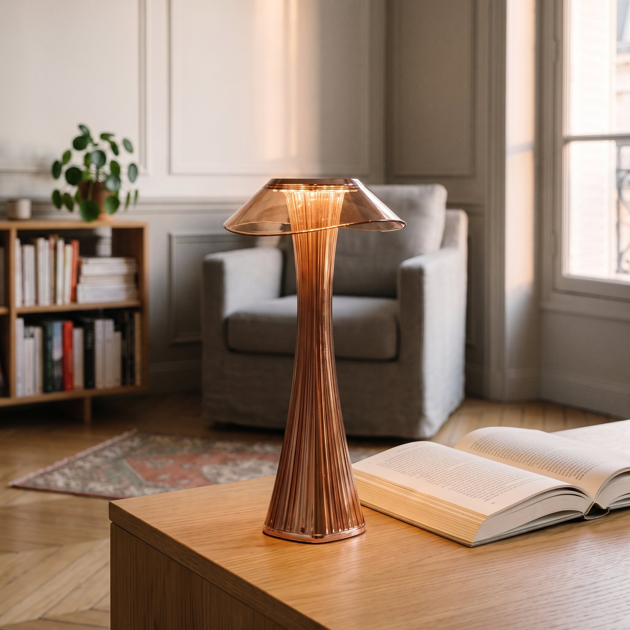 Lampe à poser rose doré allumée près d'un fauteuil de lecture Image