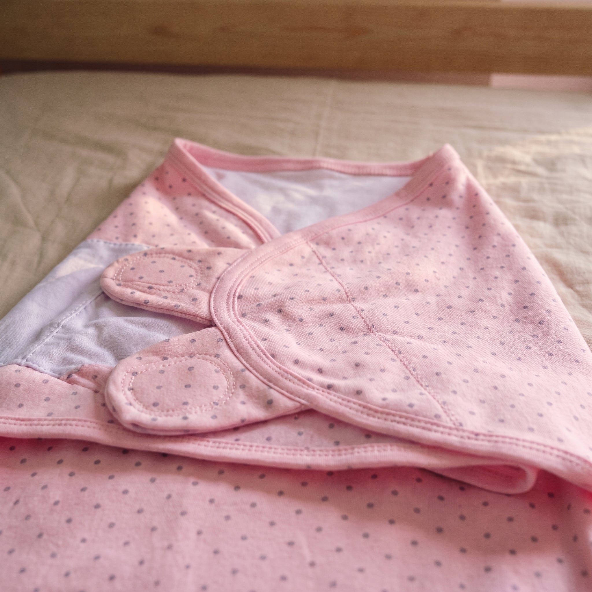Haut du sac de couchage d'emmaillotage pour bébé rose à pois gris, posé sur la couverture d'un lit d'enfant Image