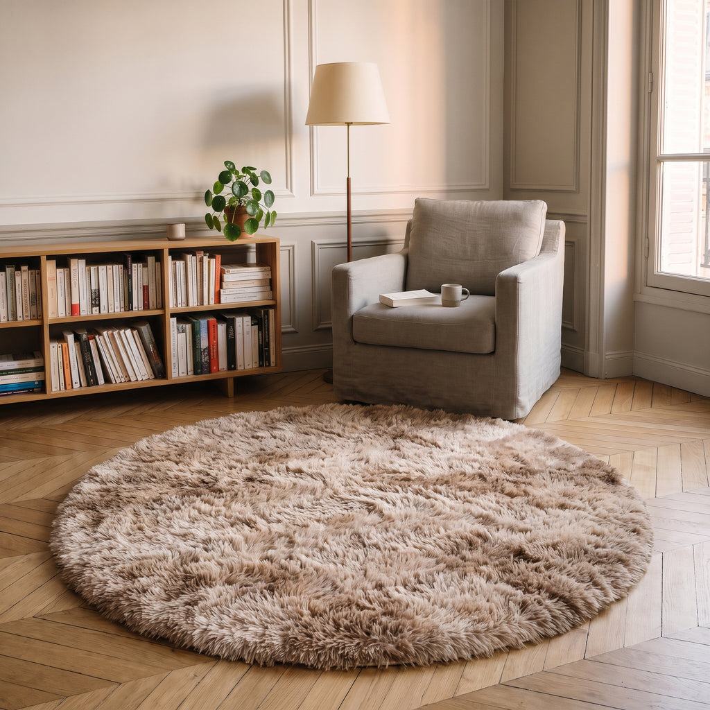 Tapis rond à poils longs coloris Beige foncé, posé devant le fauteuil d'un coin lecture