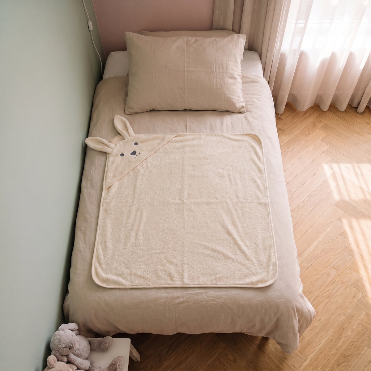 Cape de bain bebe 90 x 90 cm coloris beige, capuche lapin, depliee sur le lit d enfant