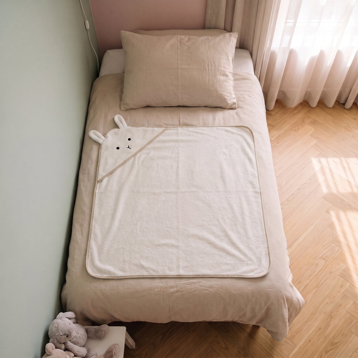 Cape de bain bebe 90 x 90 cm coloris blanc, capuche lapin, depliee sur le lit d enfant