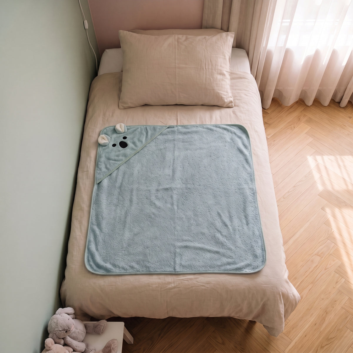 Cape de bain bebe 90 x 90 cm coloris bleu clair, capuche koala, depliee sur le lit d enfant