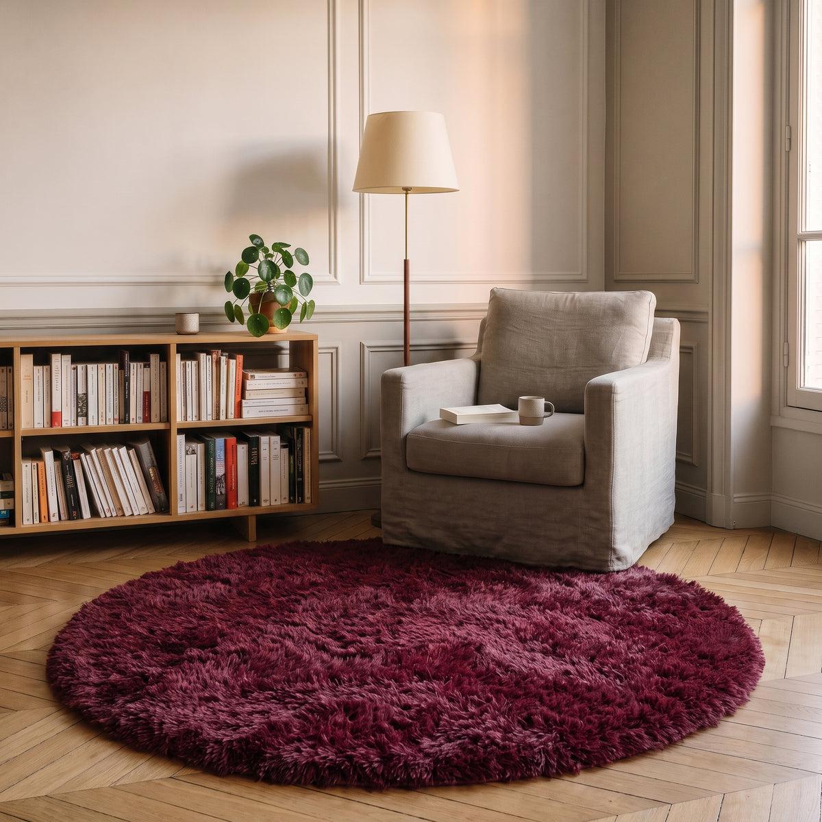 Tapis rond à poils longs coloris Bordeaux, posé devant le fauteuil d'un coin lecture