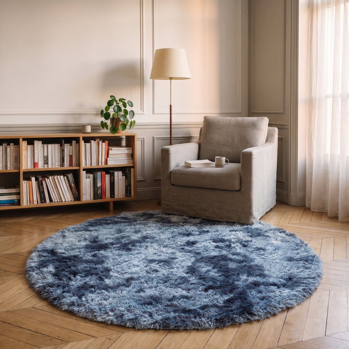 Tapis rond à poils longs coloris Gris bleu, posé devant le fauteuil d'un coin lecture