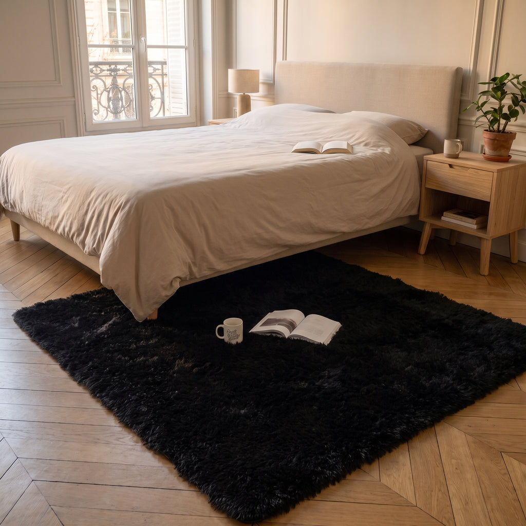 Tapis à poils longs noir devant le lit, un mug et un livre ouvert posés dessus