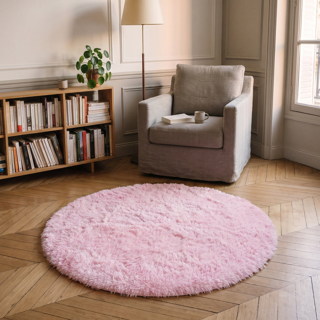 Tapis rond à poils longs coloris Rose léger, posé devant le fauteuil d'un coin lecture