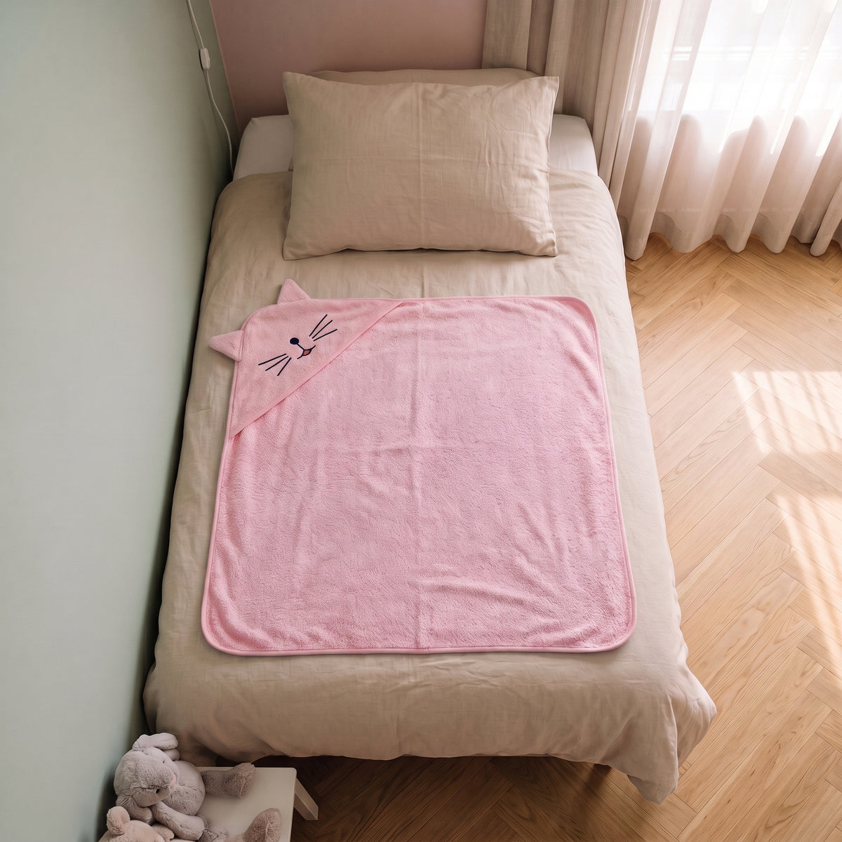 Cape de bain bebe 90 x 90 cm coloris rose, capuche chat, depliee sur le lit d enfant