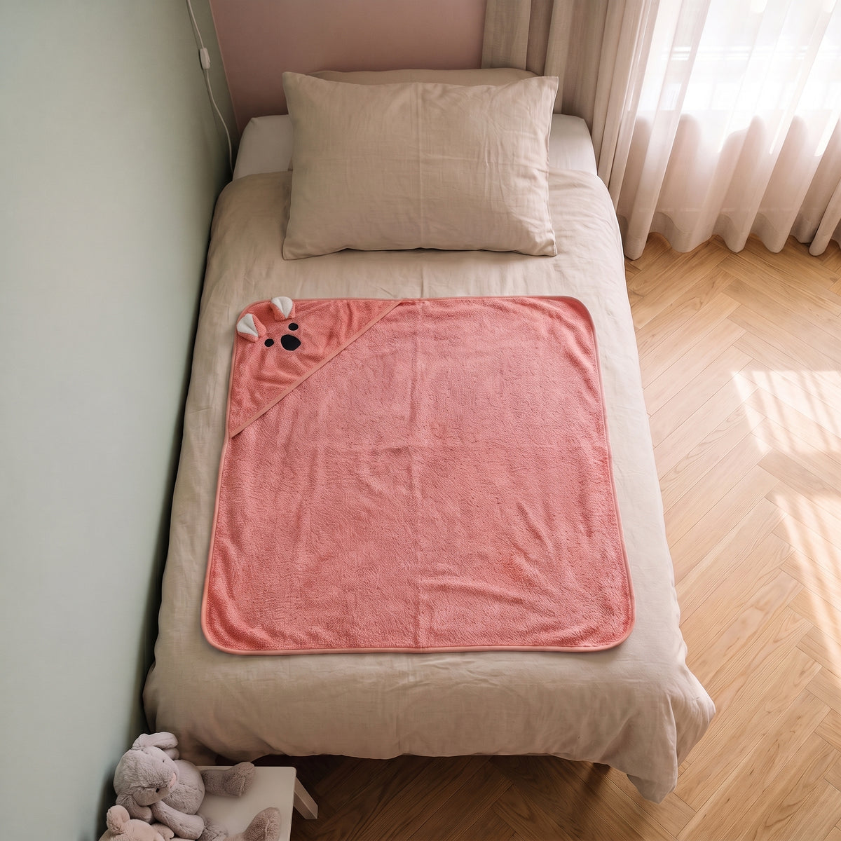 Cape de bain bebe 90 x 90 cm coloris corail, capuche koala, depliee sur le lit d enfant