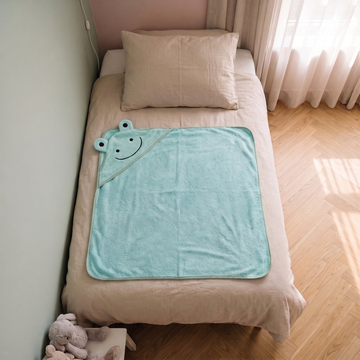 Cape de bain bebe 90 x 90 cm coloris vert d eau, capuche grenouille, depliee sur le lit d enfant