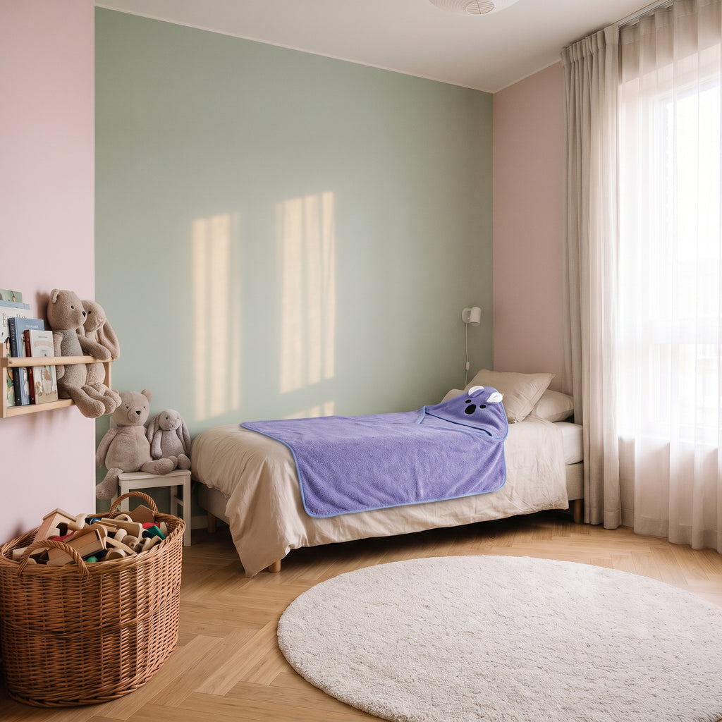 Cape de bain bébé violette à capuche animal posée sur le lit d'enfant