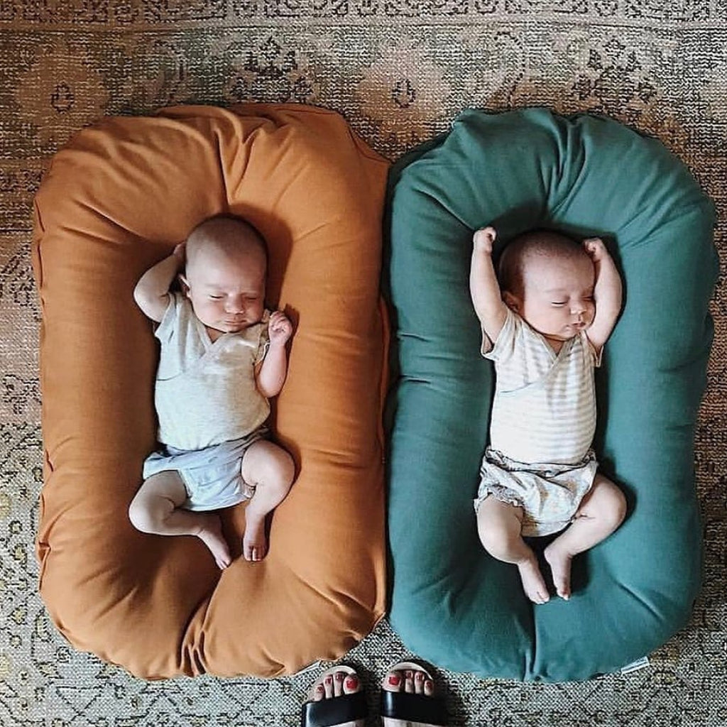 Deux bébés installés dans des coussins cocon marron et vert