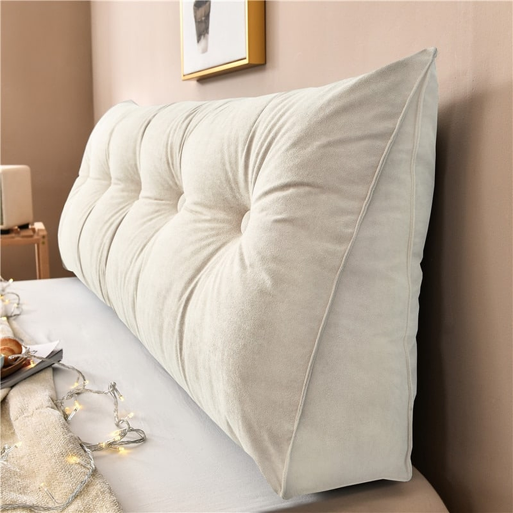 Coussin de chevet triangulaire blanc cassé posé en travers d'un lit, capitonnage et flanc visibles