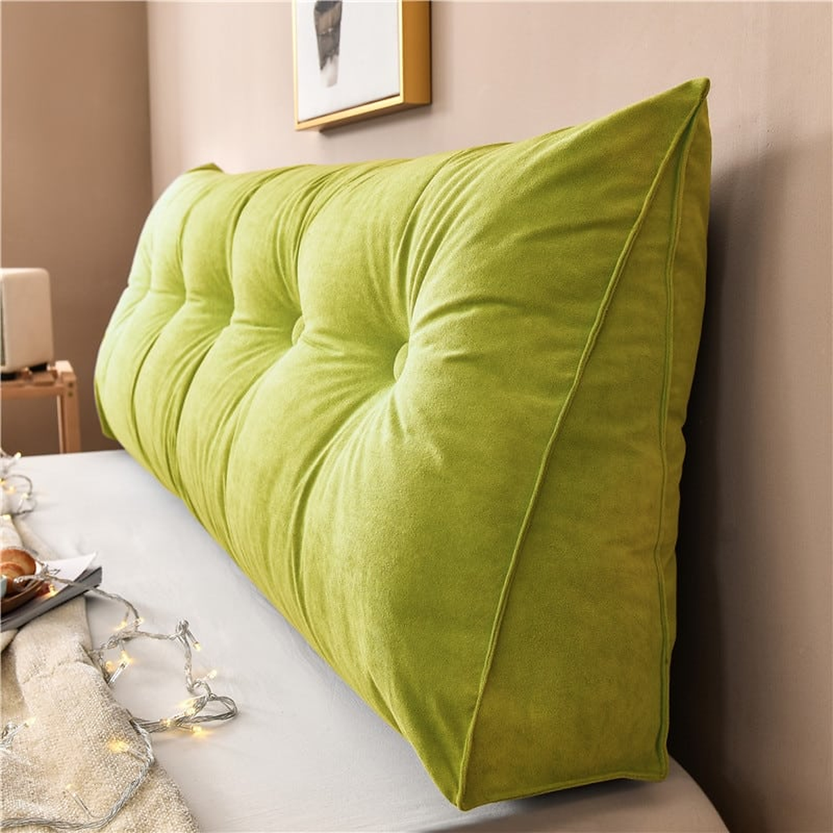 Coussin de chevet triangulaire vert citron posé en travers d'un lit, capitonnage et flanc visibles