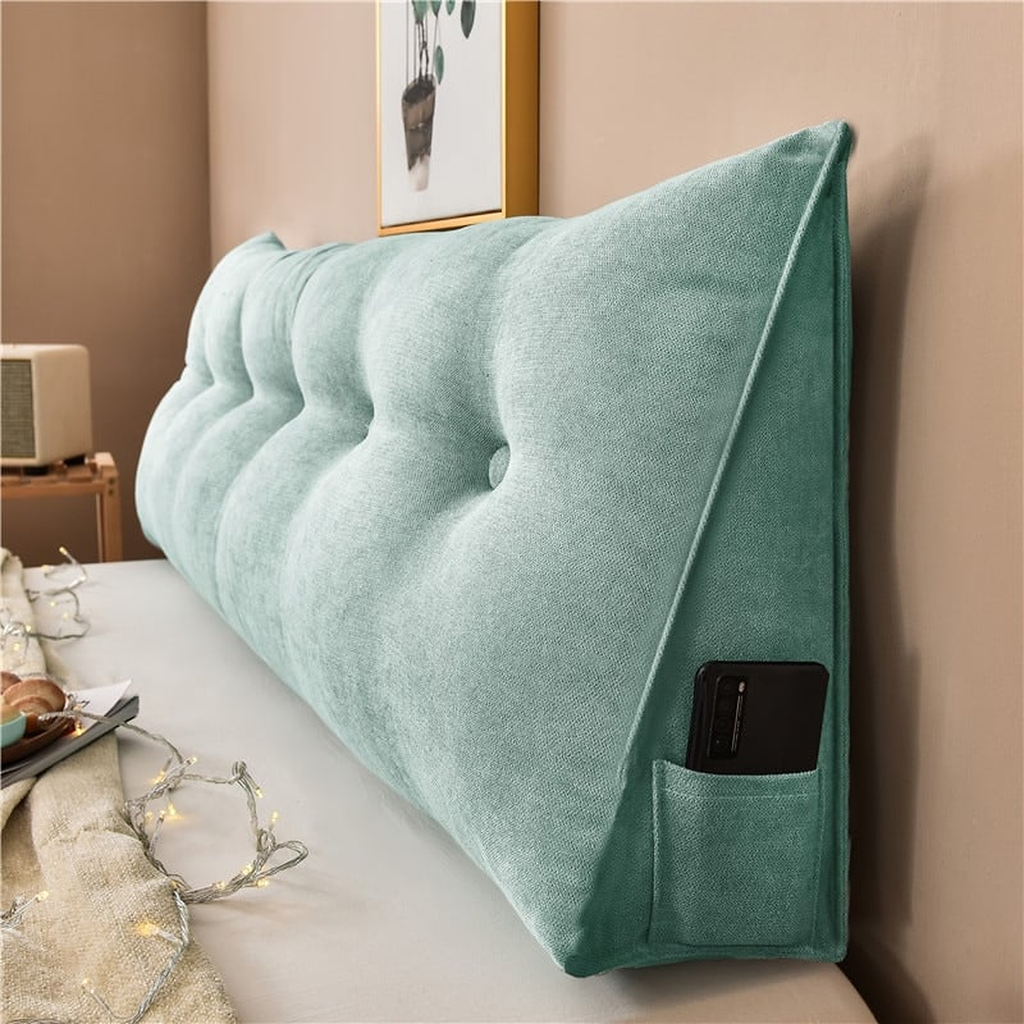 Coussin de chevet triangulaire vert céladon posé en travers d'un lit, capitonnage et flanc visibles