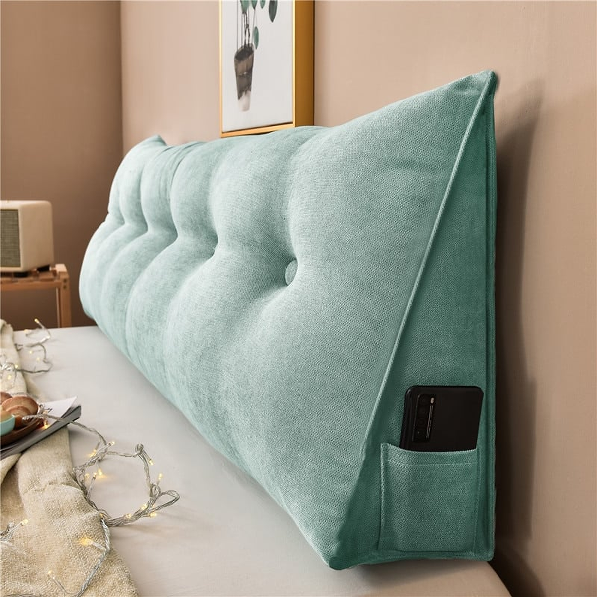 Coussin de chevet triangulaire vert céladon posé en travers d'un lit, capitonnage et flanc visibles