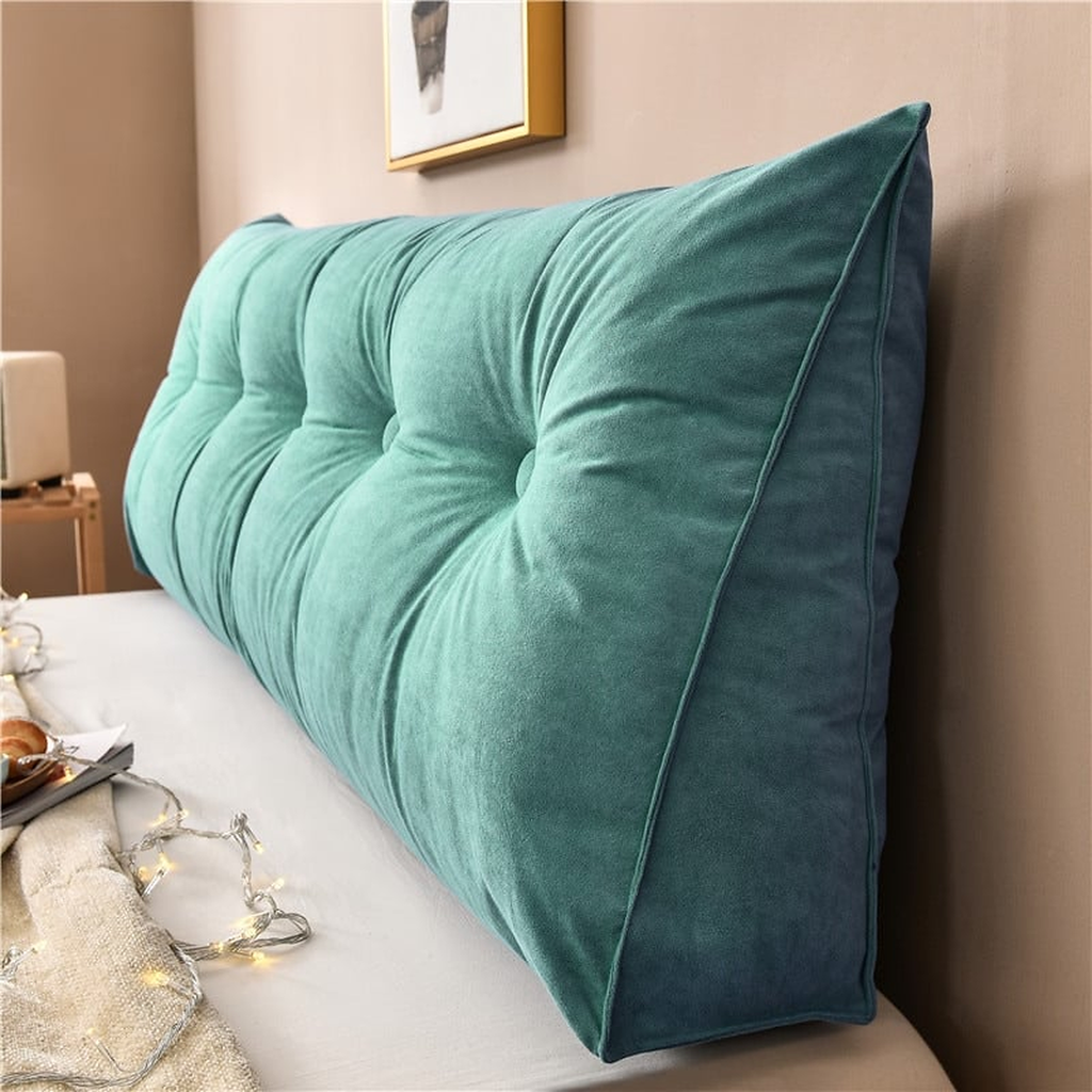 Coussin de chevet triangulaire vert d'eau soutenu posé en travers d'un lit, capitonnage et flanc visibles