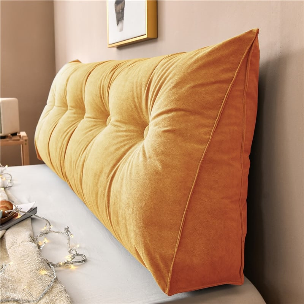 Coussin de chevet triangulaire orange terracotta posé en travers d'un lit, capitonnage et flanc visibles